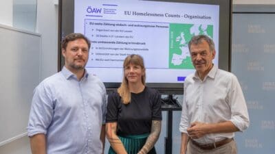 Zwei Männer und eine Frau stehen vor einer Präsentation zur EU-Zählung von Wohnungslosen in Innsbruck.