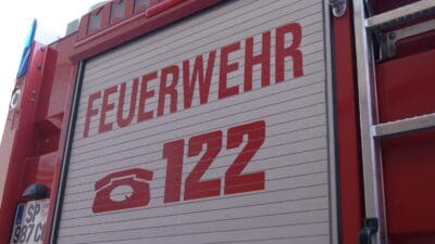 Nahaufnahme eines roten Feuerwehrfahrzeugs mit Aufschrift Feuerwehr und Notrufnummer 122 auf der Rolltür
