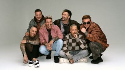 Die sechs Mitglieder der Band Electric Callboy lächeln in die Kamera vor einem grauen Hintergrund.