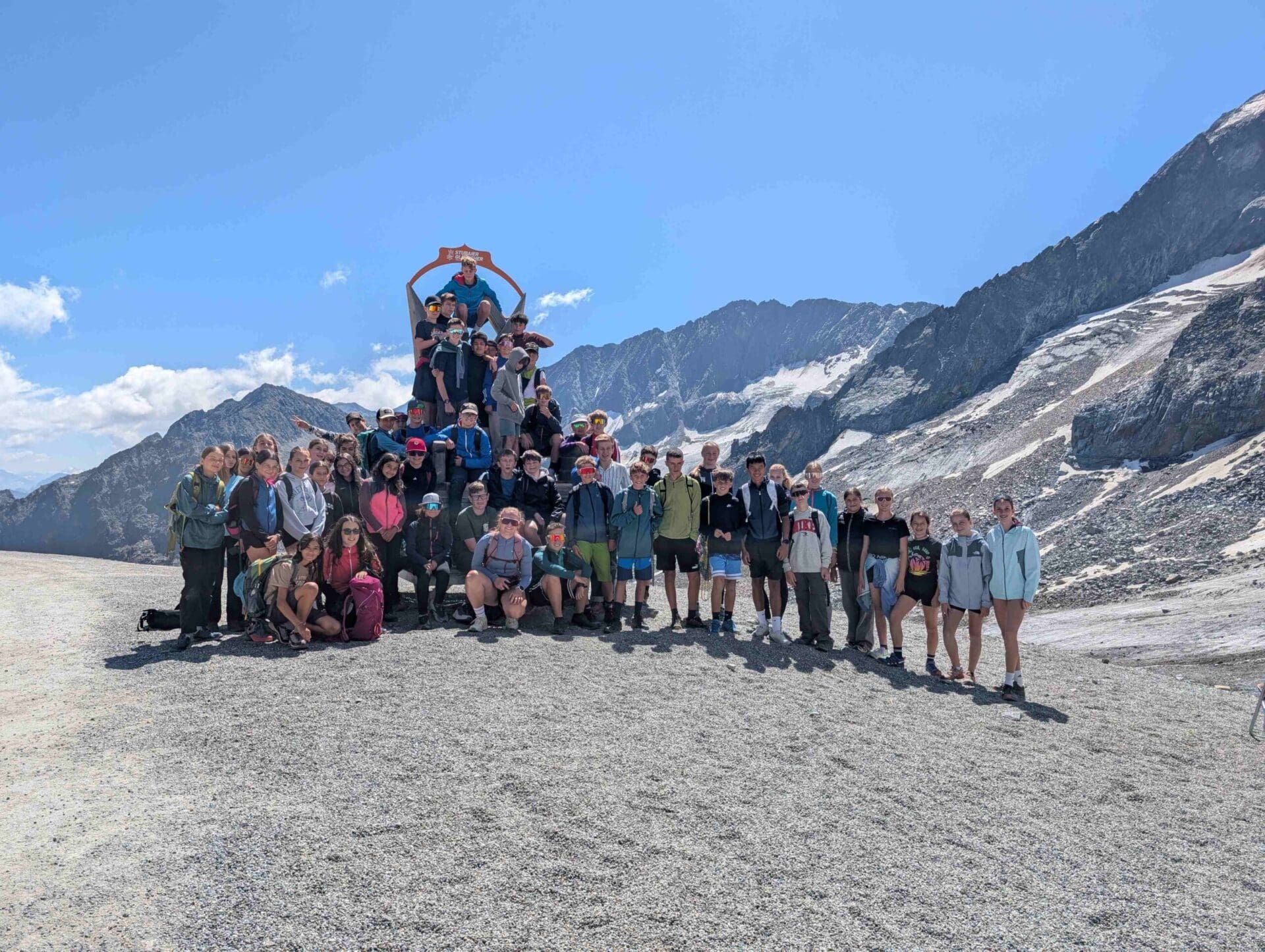 Gruppe von Jugendlichen posiert auf einem Berggipfel vor schneebedeckten Alpen