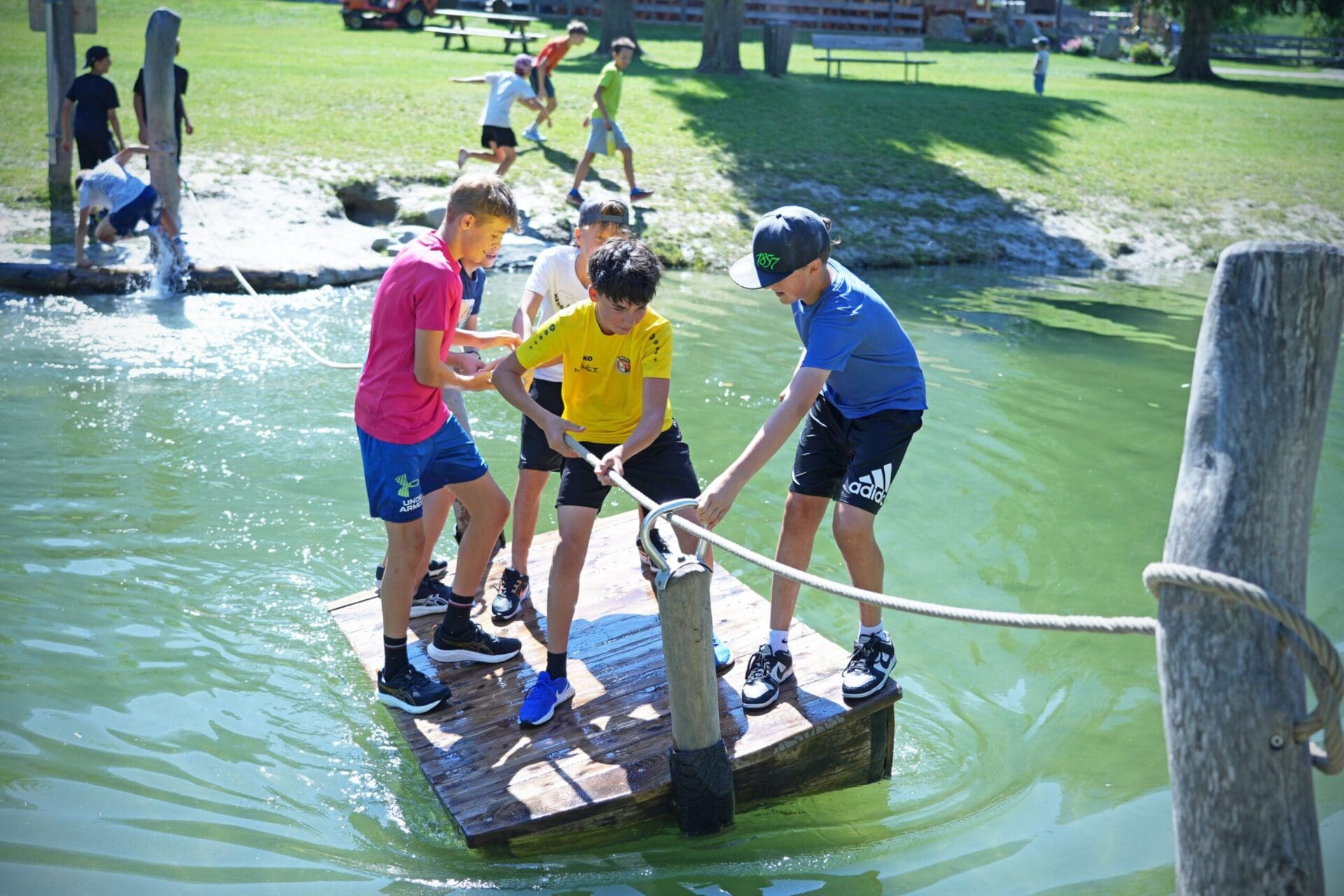 Jungen auf einem Holzsteg im Wasser ziehen gemeinsam an einem Seil.