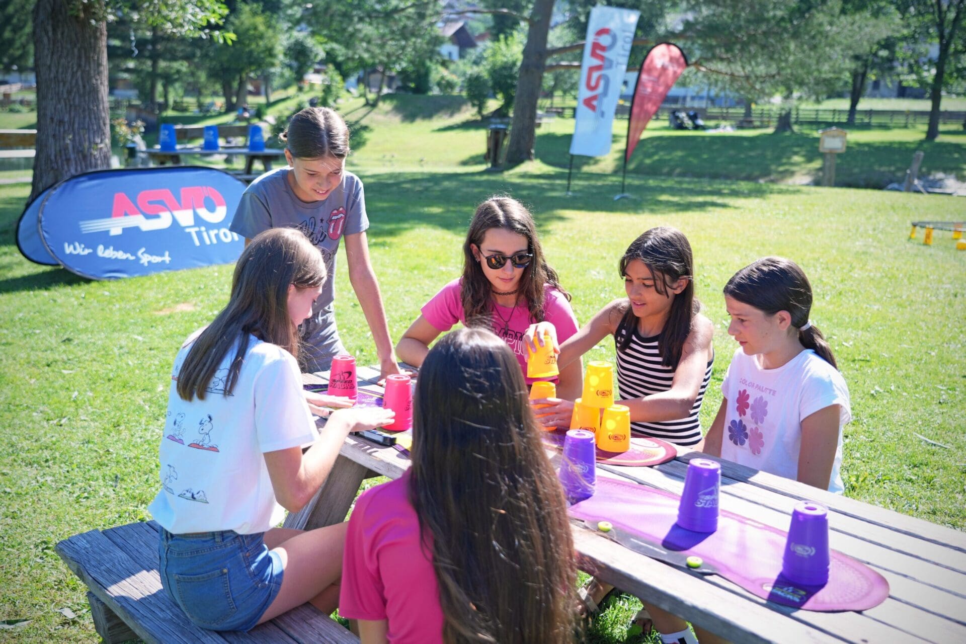 Mehrere Mädchen spielen an einem Picknicktisch im Freien mit bunten Plastikbechern ein Geschicklichkeitsspiel.