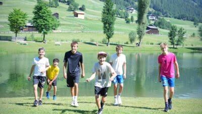 Fünf Jungen stehen lachend am Ufer eines Sees in den Bergen.
