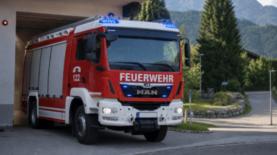 Rotes Feuerwehrfahrzeug mit blauen Blinklichtern vor einer Feuerwache in den Bergen
