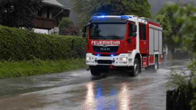 Rotes und weißes Feuerwehrauto mit Blaulicht fährt durch Regen auf nasser Straße