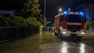 Rotes Feuerwehrfahrzeug mit Blaulicht auf überfluteter Straße im nächtlichen Regen