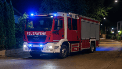 Rotes und weißes Feuerwehrfahrzeug mit blauem Blaulicht parkt nachts auf einer Straße