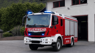 Rotes und weißes Feuerwehrfahrzeug mit aktiviertem Blaulicht vor einer Feuerwehrstation
