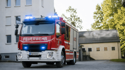 Roter und weißer Feuerwehrwagen mit leuchtendem Blaulicht vor einem Gebäude