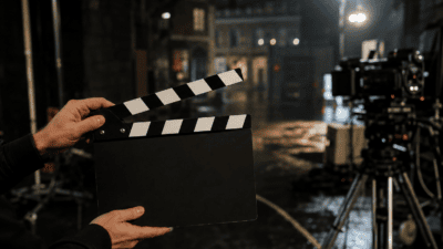 Eine Hand hält eine schwarz-weiße Filmklappe vor einer Filmkamera auf einem nächtlichen Set.