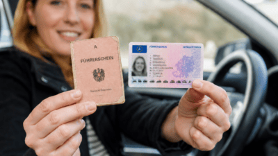 Eine Frau im Auto hält einen alten Papierführerschein und einen neuen Kartenführerschein.