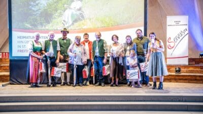 Gruppe von Menschen in Tracht auf einer Bühne vor einer großen Leinwand.