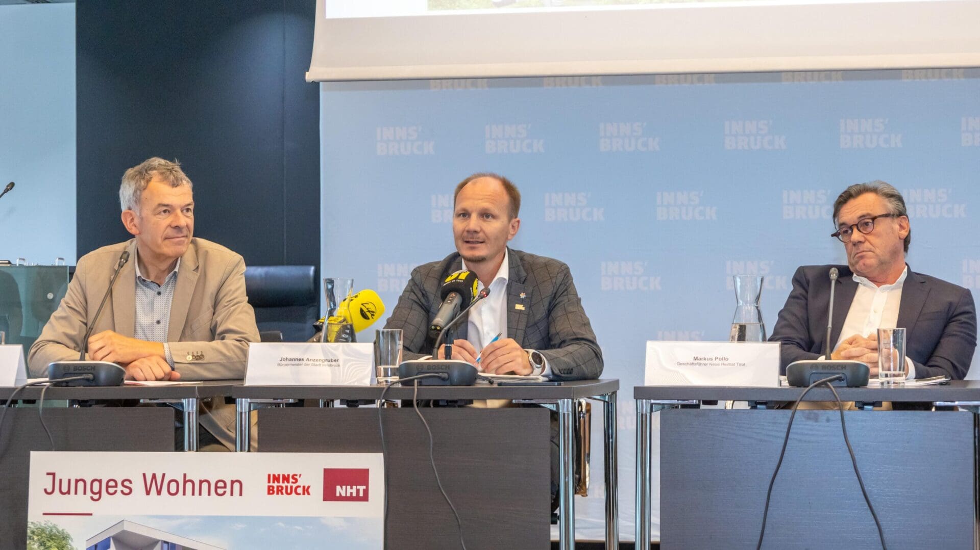 Drei Männer in Anzügen sitzen an einem Tisch bei einer Pressekonferenz in Innsbruck.