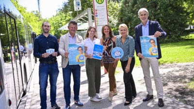 Sechs Personen halten Plakate und Schilder zur KMG-Kundenbefragung vor einem Bus an der Universitäts-Haltestelle.
