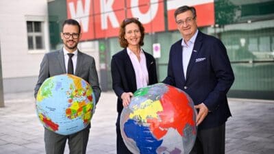 Drei Personen in Businesskleidung halten vor dem WKÖ-Gebäude zwei große Weltkugeln