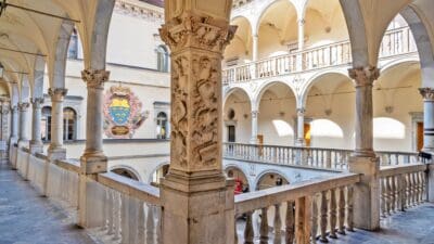 Verzierter Innenhof mit steinernen Säulen, Arkaden und Wappen an der Wand