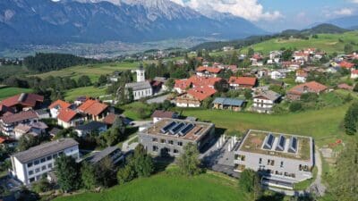 Luftaufnahme des Ortes Lans mit Kirche, Häusern und schneebedeckten Bergen im Hintergrund