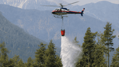 Polizeihubschrauber lässt Löschwasser über einem bewaldeten Berggebiet ab