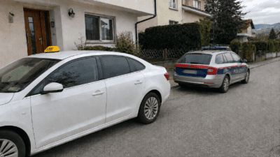 Weißes Taxi mit gelbem Dachschild und Polizeiwagen vor einem Wohnhaus