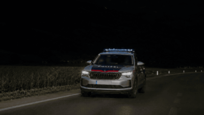 Silbernes Polizeiauto mit blauem Blaulicht auf nächtlicher Landstraße vor dunklen Bergen