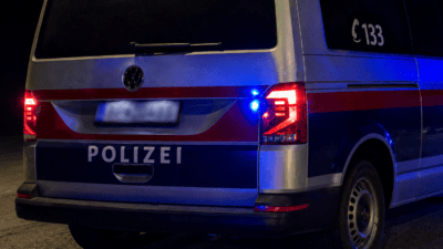 Heckansicht eines silbernen und blauen Polizeivans mit rotem Streifen und leuchtendem Blaulicht bei Nacht