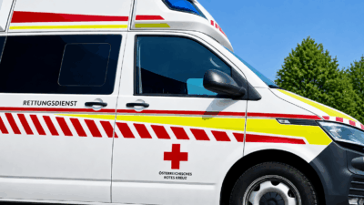 Weißer Rettungswagen des Österreichischen Roten Kreuzes mit roten und gelben Streifen unter blauem Himmel
