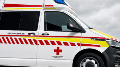 Weißer Rettungswagen des Österreichischen Roten Kreuzes mit rotem Kreuz und Warnstreifen bei bewölktem Himmel