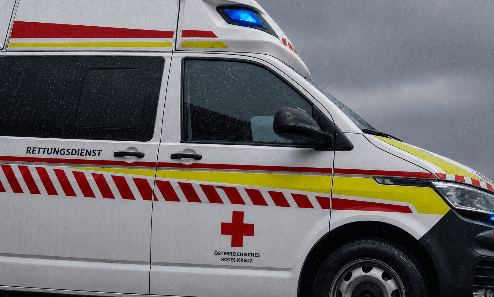 Weißer Rettungswagen des Österreichischen Roten Kreuzes mit rotem Kreuz und Streifen im Regen