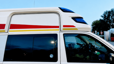 Seitenansicht eines weißen Rettungswagens mit roten und gelben Streifen im hellen Sonnenlicht