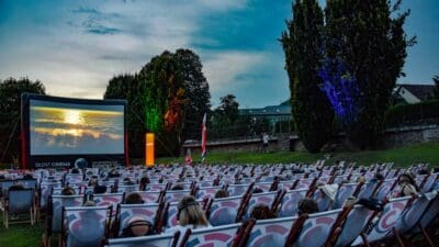 Zuschauer in bunten Liegestühlen mit Kopfhörern vor großer Leinwand im Freien bei Dämmerung