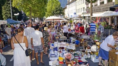 Besucher betrachten Porzellan und Waren an Ständen eines Flohmarkts auf einer Straße.