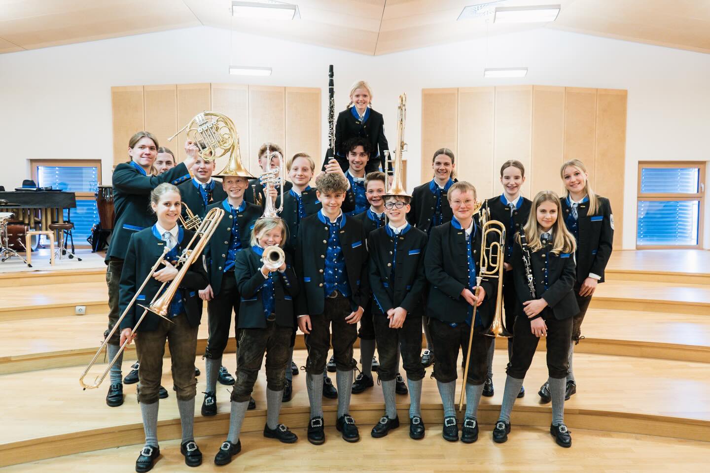 Gruppe junger Musiker in Tracht mit Blechblasinstrumenten auf Holzstufen in einem Saal