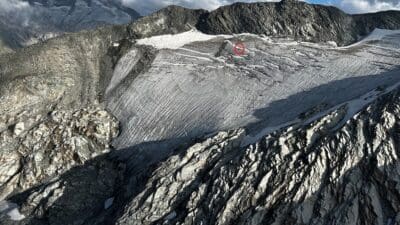 Weitläufiger vereister Gletscher mit Spalten und umliegenden Bergmassiven, roter Kreis markiert eine Stelle auf dem Eis.