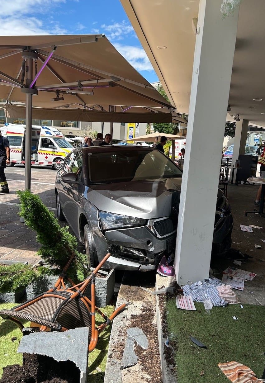 Beschädigtes graues Auto nach Unfall gegen Säule in überdachtem Gastgarten mit umgestürzten Stühlen