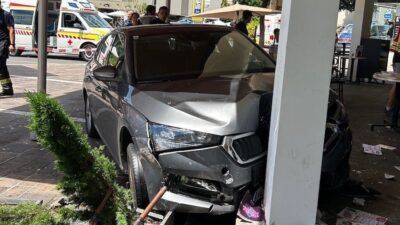 Ein stark beschädigtes graues Auto steht nach dem Aufprall an einer Säule unter großen Sonnenschirmen.