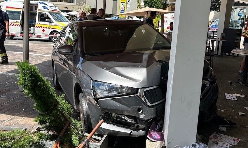 Ein stark beschädigtes graues Auto steht nach dem Aufprall an einer Säule unter großen Sonnenschirmen.