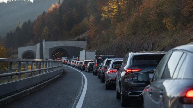 Lange Schlange von Autos auf kurviger Autobahn vor Tunnel in herbstlicher Berglandschaft