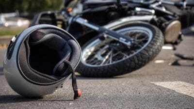Grauer Motorradhelm liegt auf der Straße vor einem umgestürzten Motorrad nach einem Unfall