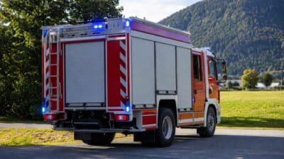 Heckansicht eines Feuerwehrfahrzeugs mit blauen Warnlichtern und roten Streifen vor Bergen