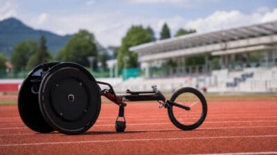 Ein schwarzer Rennrollstuhl mit rotem Rahmen auf einer roten Laufbahn in einem Stadion