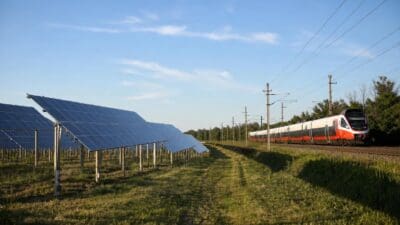 Reihen von Solarpaneelen neben einer Bahnstrecke mit einem vorbeifahrenden Zug