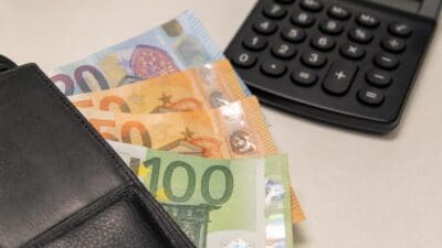 Ein schwarzes Portemonnaie mit Euro-Banknoten und ein Taschenrechner auf hellem Untergrund