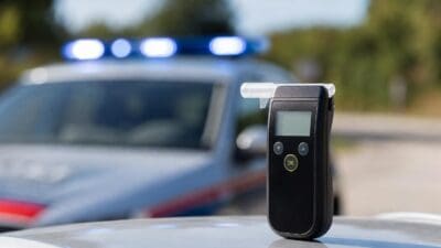 Ein Alkoholtester steht auf der Motorhaube eines Autos vor einem Polizeifahrzeug mit Blaulicht