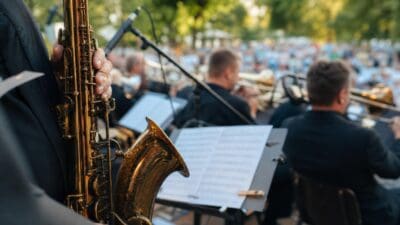 Ein Musiker haelt ein goldenes Saxophon vor einer Big-Band-Buehne mit Publikum im Hintergrund.