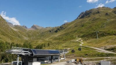 Talstation einer Seilbahn mit Gondeln vor grünen Bergen unter blauem Himmel