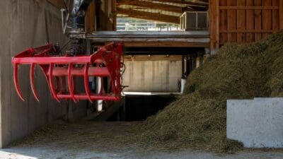 Rote Greifzange eines Krans in einer Scheune mit großem Heuhaufen