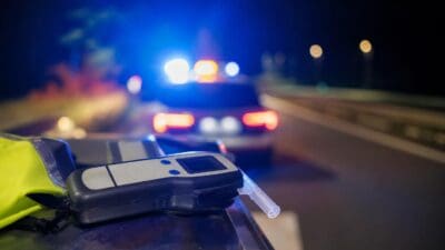 Alkoholtester und Warnweste liegen nachts vor einem Polizeiauto mit Blaulicht