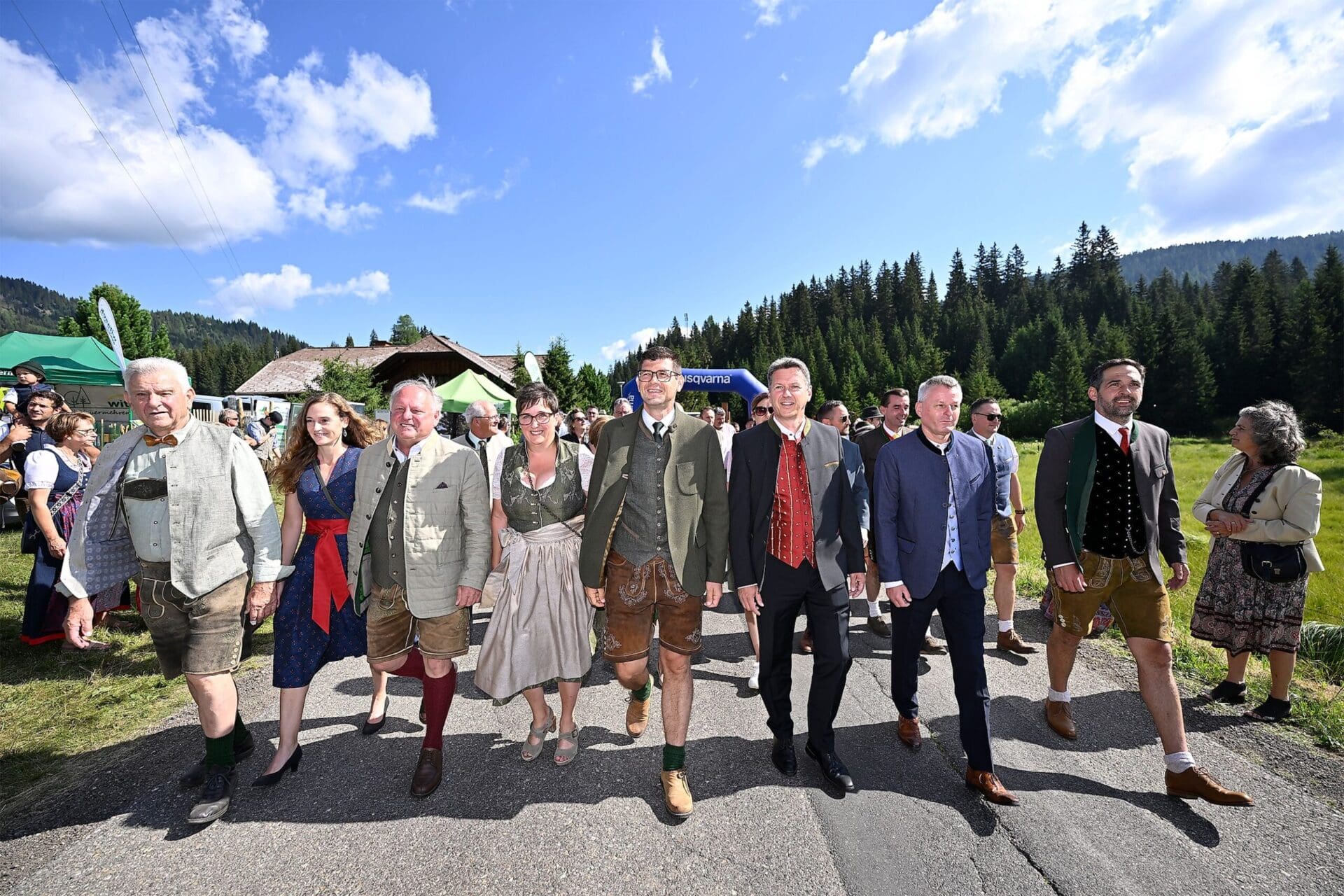 Gruppe von Menschen in traditioneller Tracht geht auf einer Straße vor Bergen