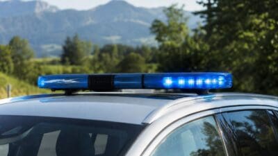 Blaues Blaulicht auf dem Dach eines silbernen Polizeifahrzeugs vor Berglandschaft