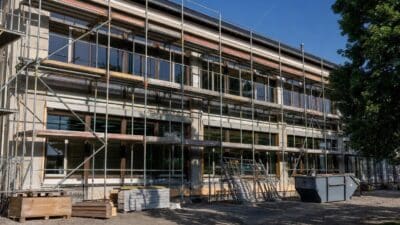 Mehrstöckiges Gebäude mit umfangreichem Gerüst und Baustellenmaterialien auf einem Sandplatz